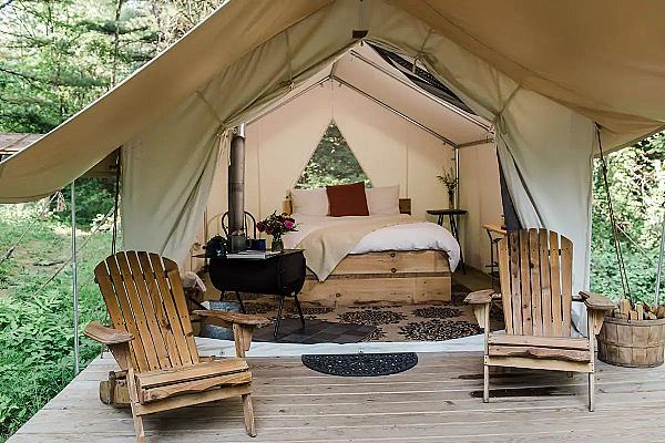 platform tent set with two Adirondack chairs, bed and wood stove