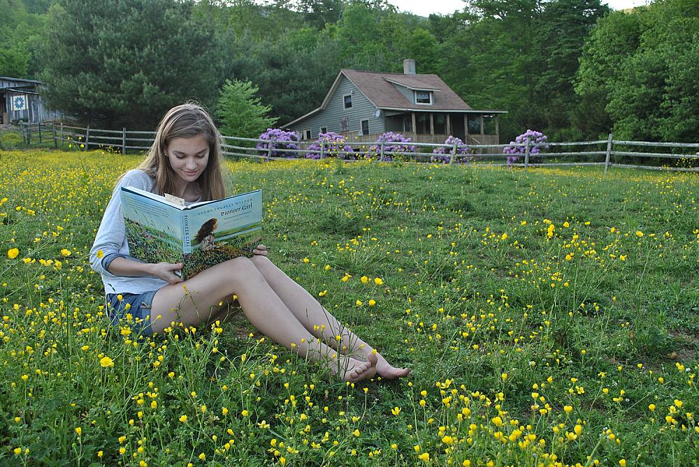 Child reading a book in the pasture in front of the Willet Pond Farm House