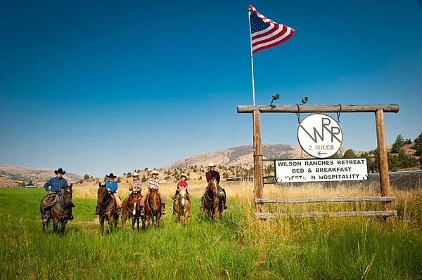 People riding horses in open fields with mountains in the background