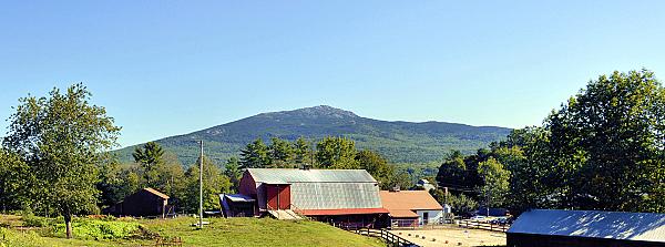red barn with riding ring and mountain behind
