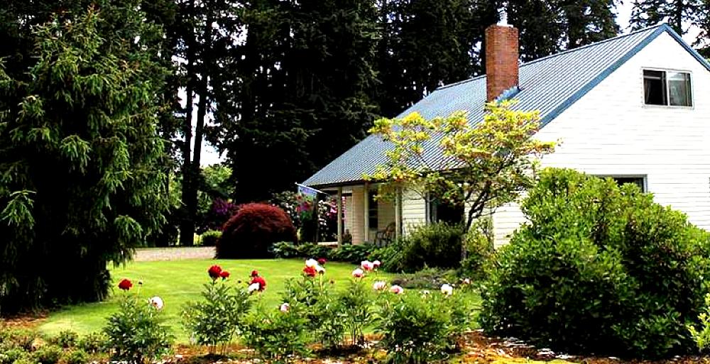 Featured Image - white farm house with flower beds and trees surrounding it