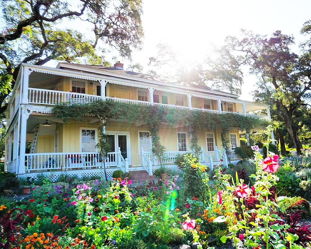 Featured Image - yellow two story house with white deck rails and garden in front