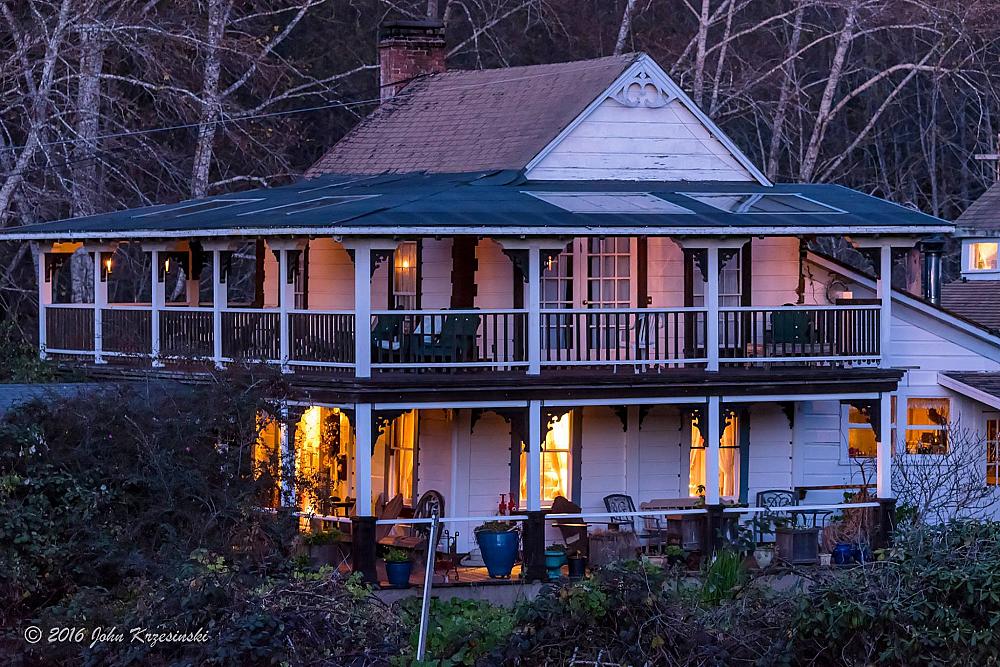 ranch house lit up at night with verandas on upper and lower floors