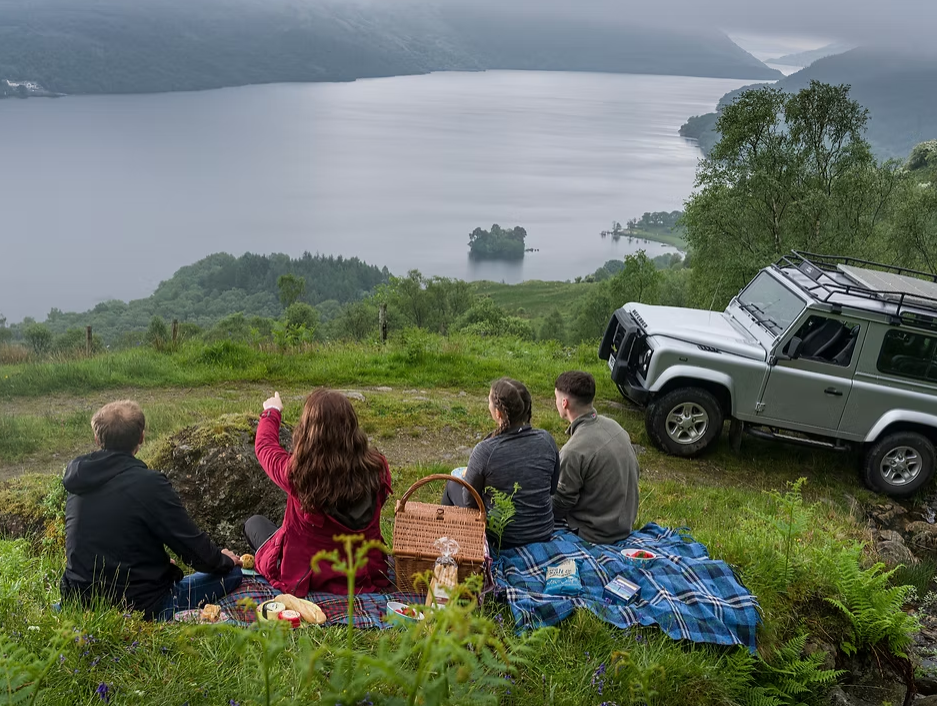 People having a picnic next to a Range Rover over looking a loch and farm in Scotland