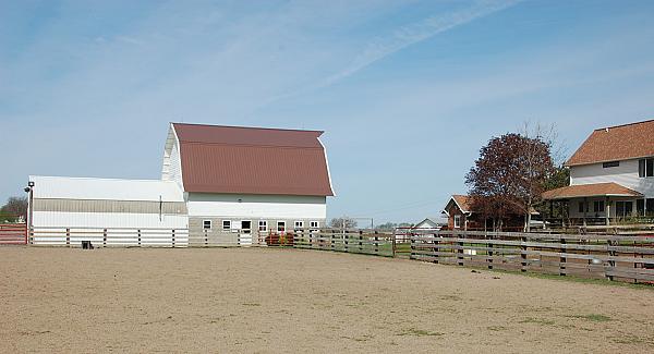 The 1930s white barn with red roof and farm house over to the right.. Arena in foreground.  