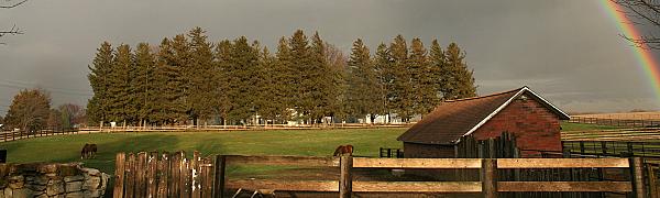 rainbow over a red barn with trees in the distance