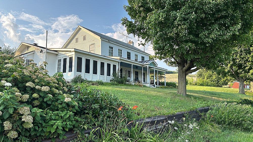 white farmhouse on a hill with white hydrangea bush in front