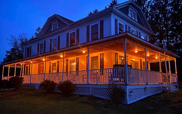 Historic white farm house at dusk with lights on the covered porch