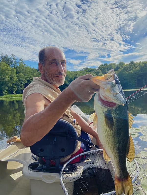a man holding a fish, just caught in a boat on a lake