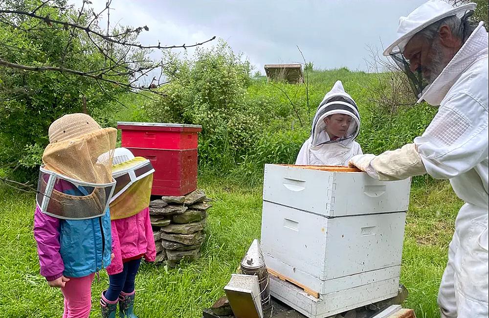 an adult and youth, dressed in bee keeping attire  learning about beekeeping as they stand around a bee hive