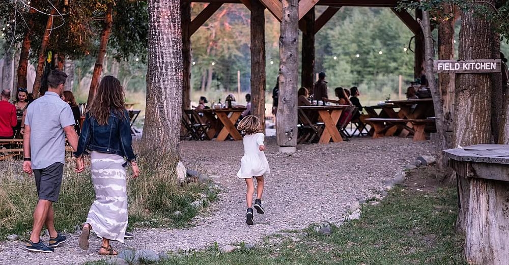 couple walking into the field kitchen which is in a wooded area with tables set up and people dining