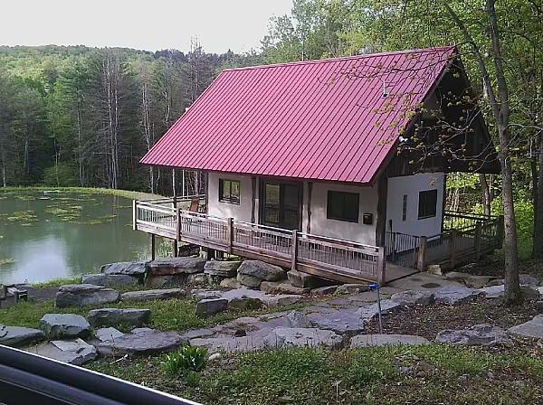 cabin with red roof facing over a pond