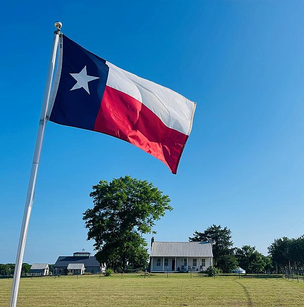 Texas flag with cottage and barn in background
