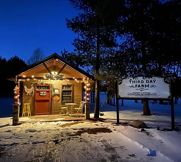 Third Day Farm store at night with white lights on the covered porch and the business sign out front