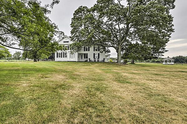 white farm house surrounded by trees with pergola in background