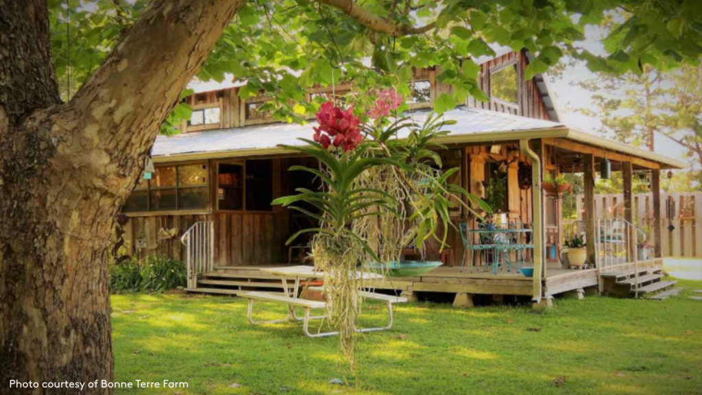An image of the cottage at Bonne Terre Farm with trees and gardens surrounding the two story cabin with a covered front porch