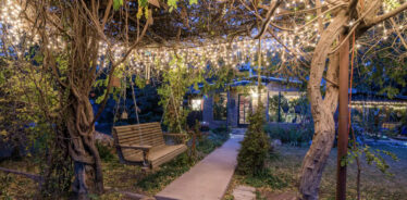 a canopy of trees and lights with a swinging bench and a cabin i nthe background set at night