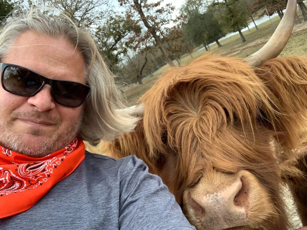 man with red Scottish Highland cow looking over his shoulder