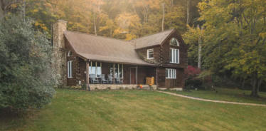2 story brown farmhouse with trees surrounding it
