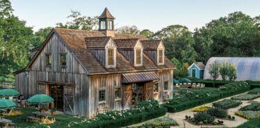 a wooden house with gardens and a greenhouse in the background